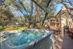 A hot tub surrounded by trees and a patio area with outdoor furniture.
