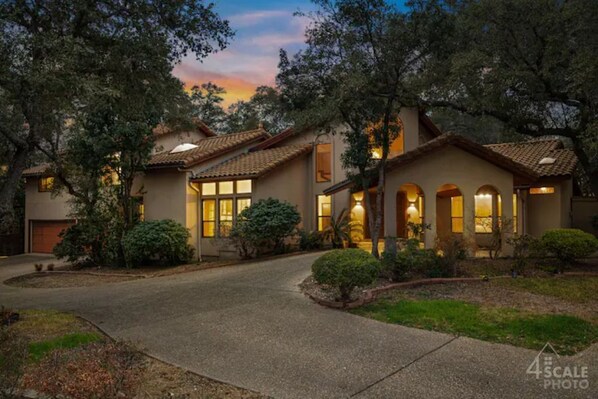 A two-story house with a driveway, surrounded by trees and well-maintained landscaping.
