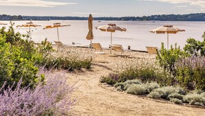 A beach with sun loungers and umbrellas, a sandy path, and a view of the water. - Silver Sands Motel & Beach Bungalows (Greenport)