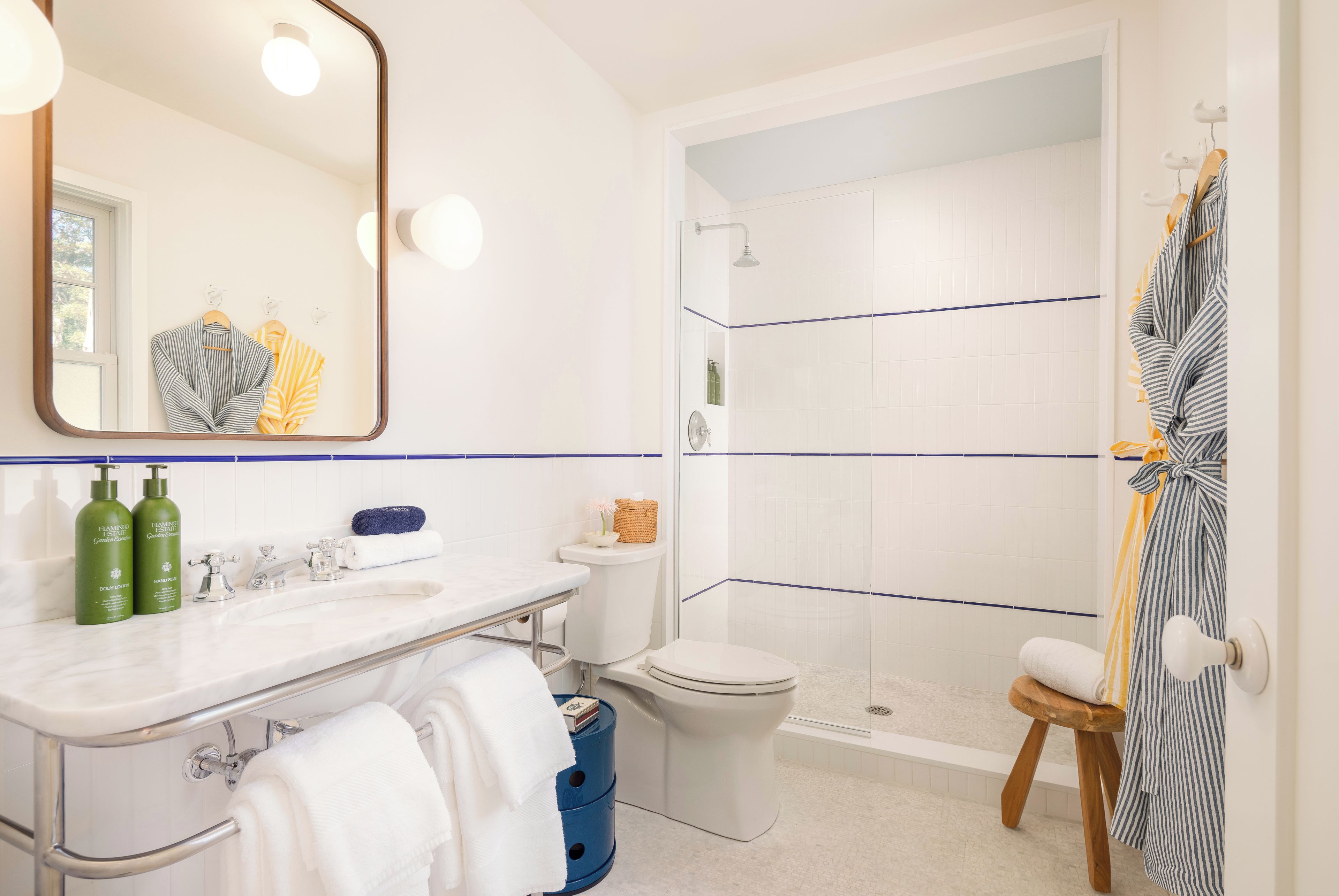 Ein modernes Badezimmer mit Waschbecken, Spiegel und Toilette in Weiß. Ein Duschbereich mit Glastür und einer Holzbank.