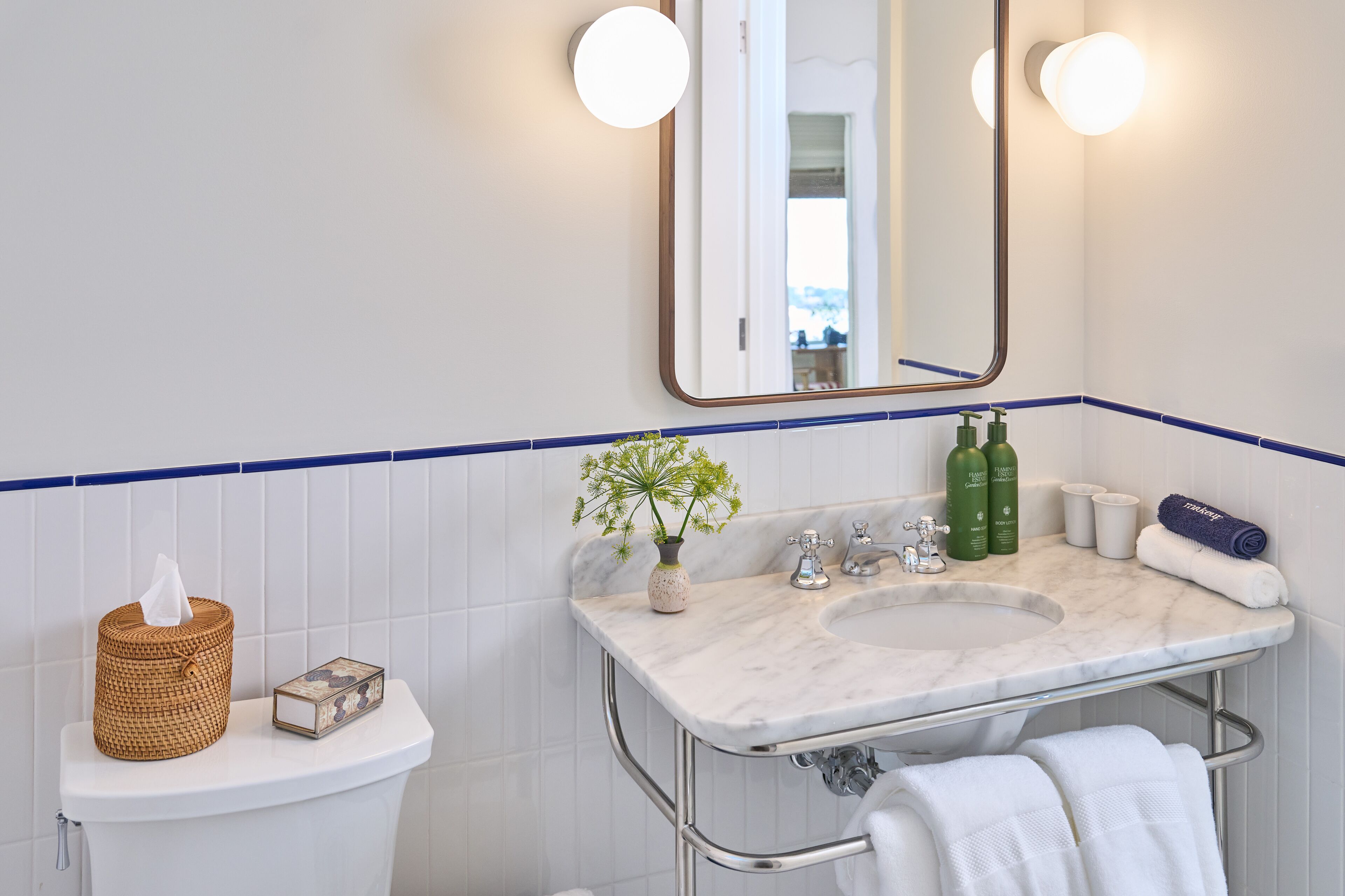 A bathroom with a white toilet, a sink with a marble countertop, a mirror, and a towel rack.