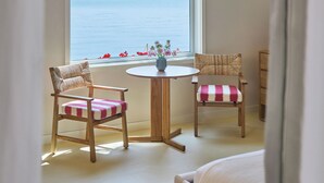 A room with a bed, two wicker chairs with checkered cushions, a small round table with a vase of flowers, and a view of a lake through a window with a bamboo blind. - Silver Sands Motel & Beach Bungalows (Greenport)