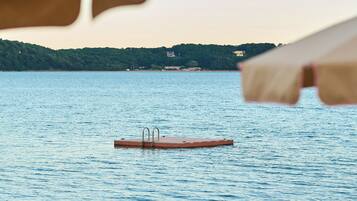 A beach with a wooden dock extending into calm water, surrounded by beach chairs and umbrellas.