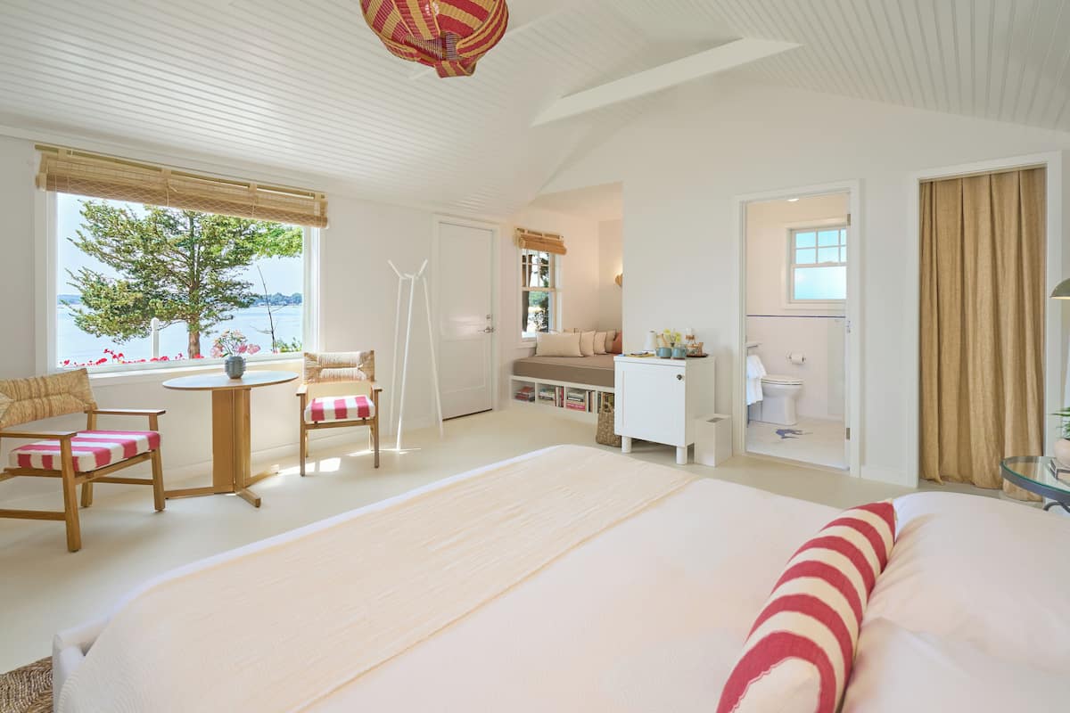 A spacious bedroom with a large bed, a sitting area with chairs, a small table, and a view of the outdoors.
