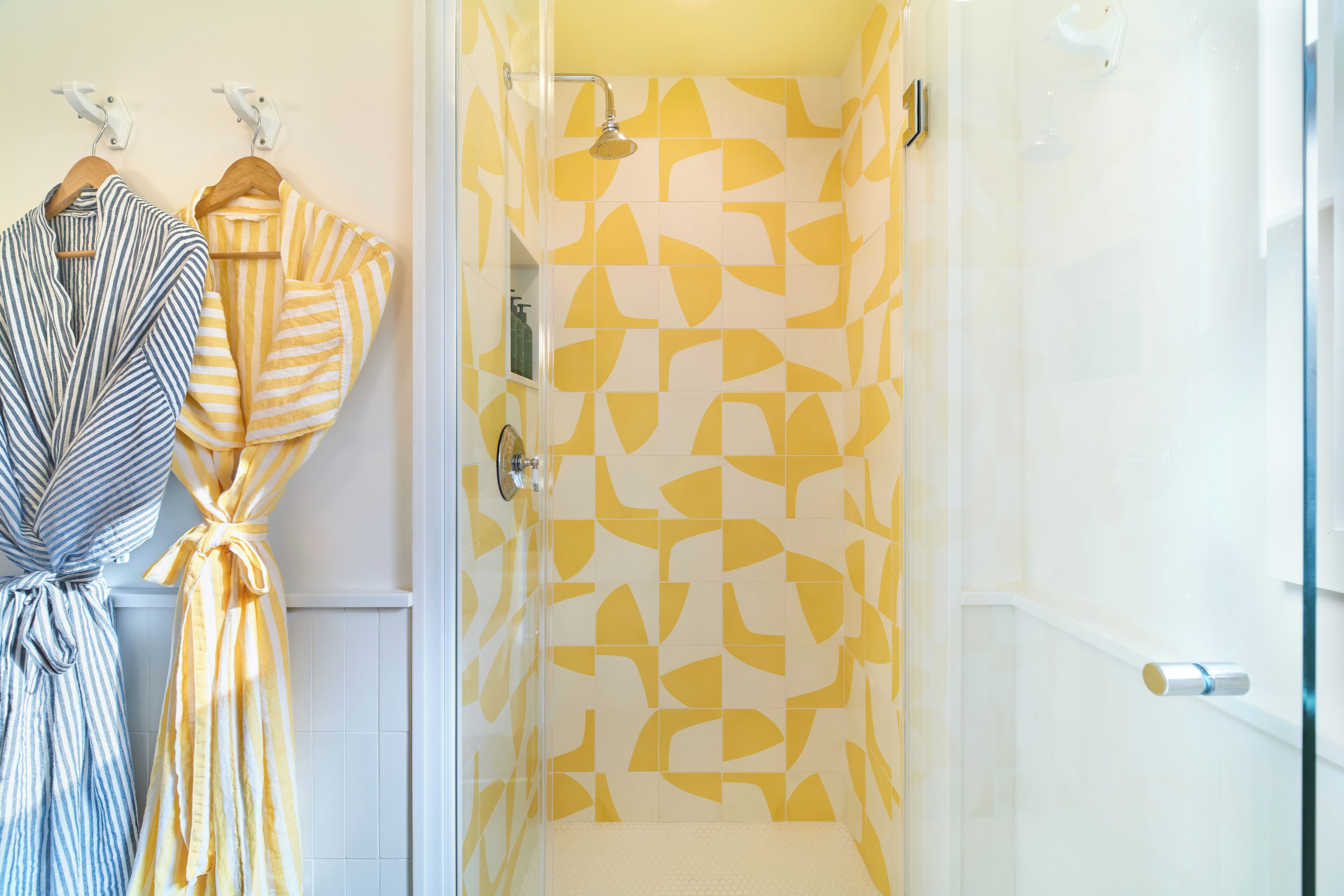 A bathroom with a shower and two bathrobes hanging on a rack.