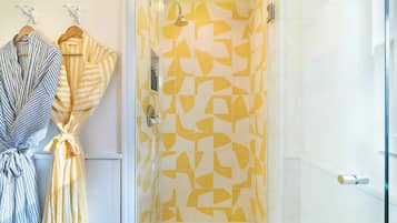 Un baño con ducha y dos albornoces colgados en un perchero.