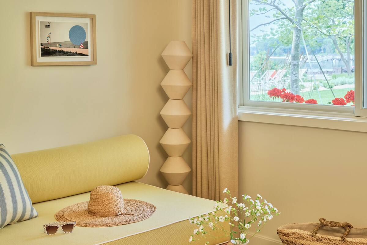 A cozy room with a sofa, a wooden table, a wicker basket, and a window with a view of trees and flowers.