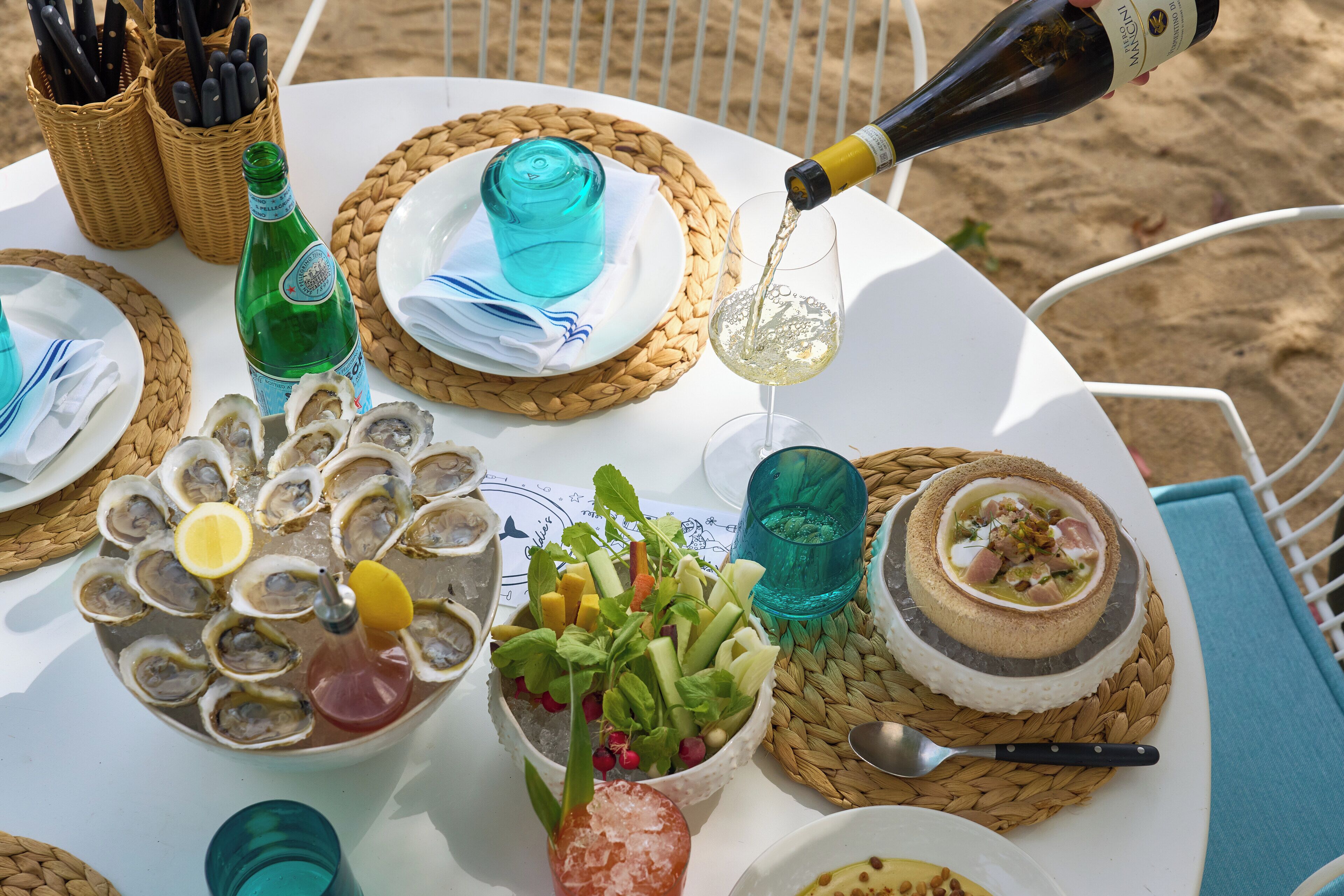 A table set with oysters, a salad, and a dessert, with a bottle of champagne being poured.