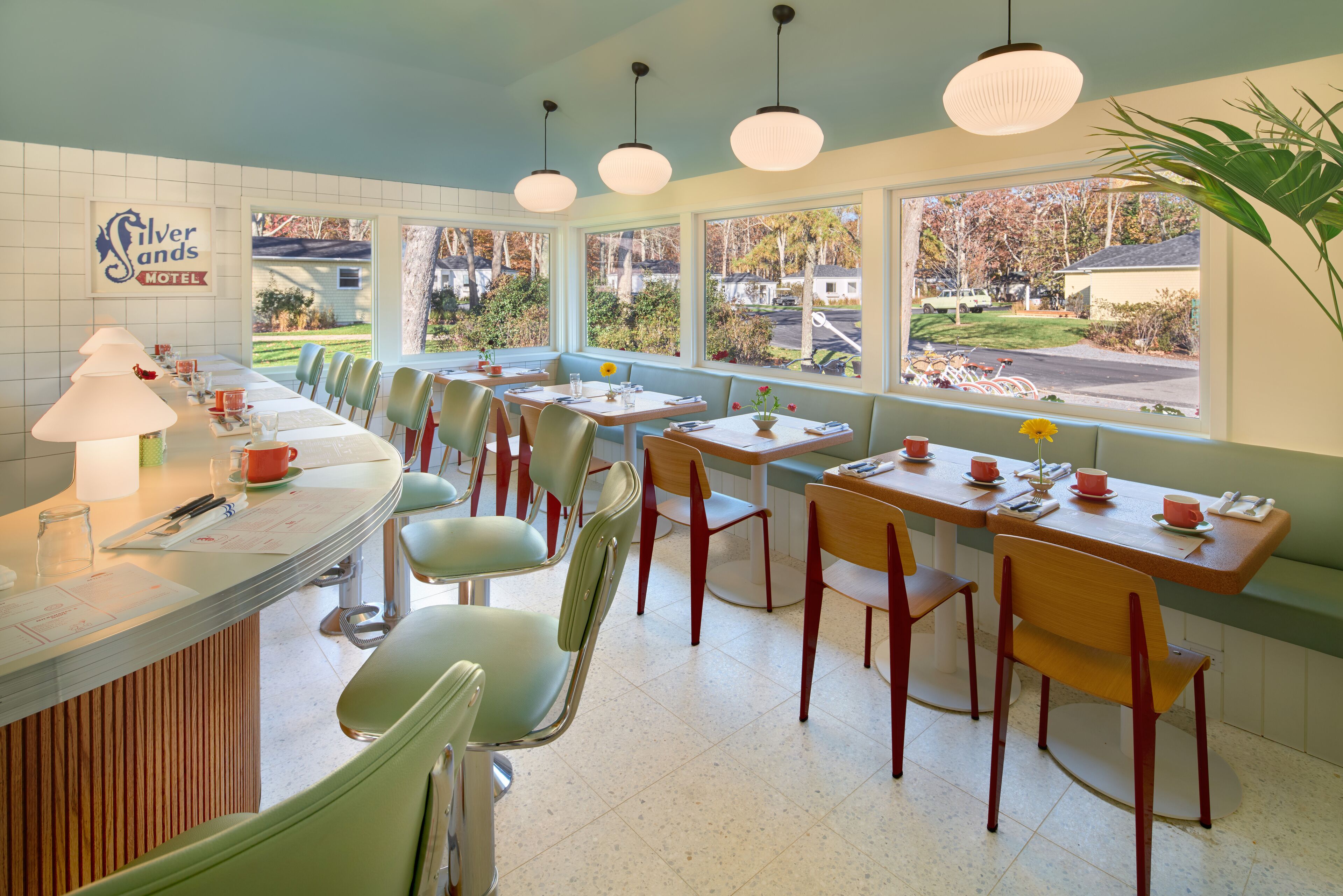A diner with a counter, booths, and tables. There are chairs and a plant.