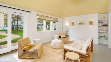 A modern living room with a large window, a sofa, a chair, a round table, and a bookshelf.