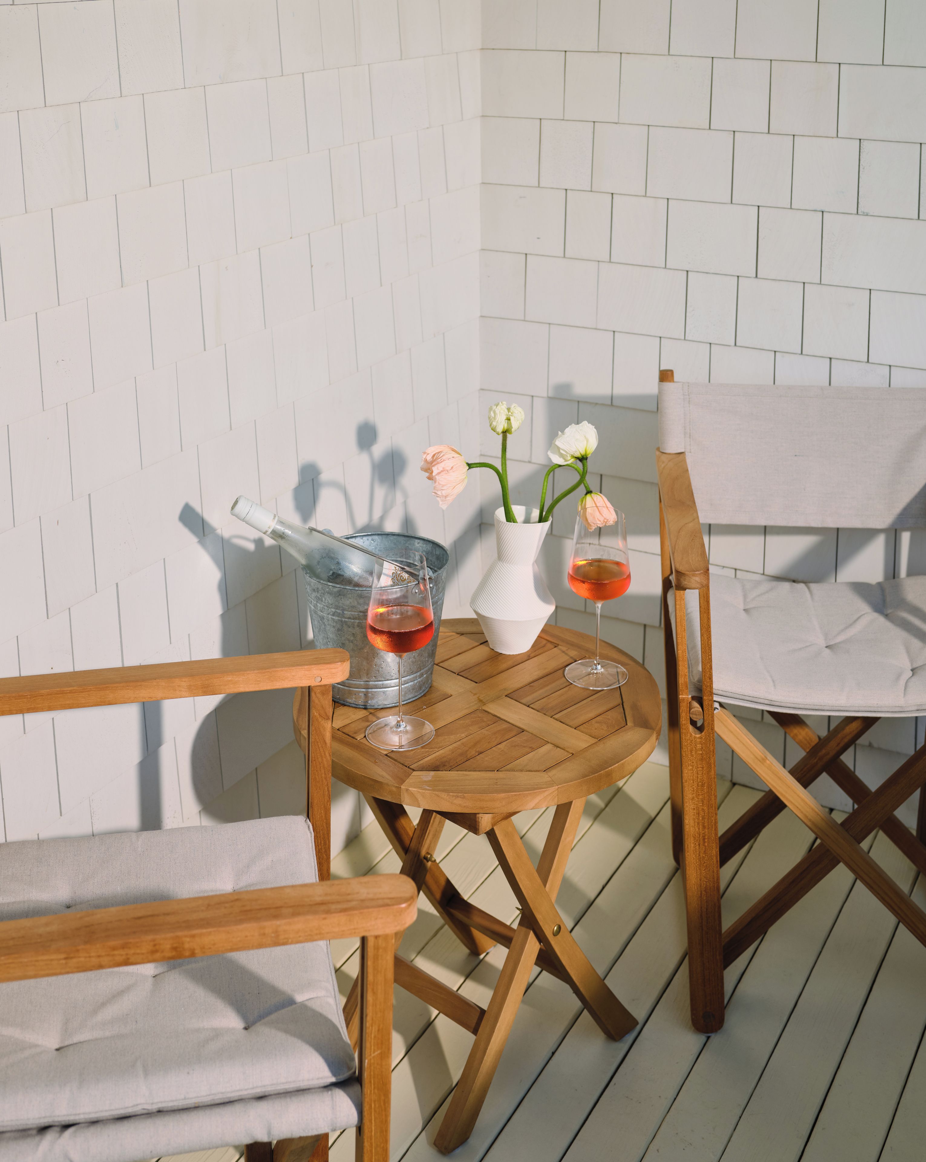 A wooden table with two wine glasses and a vase with flowers, set against a white brick wall.
