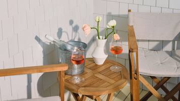 A wooden table with two wine glasses and a vase with flowers, set against a white brick wall.