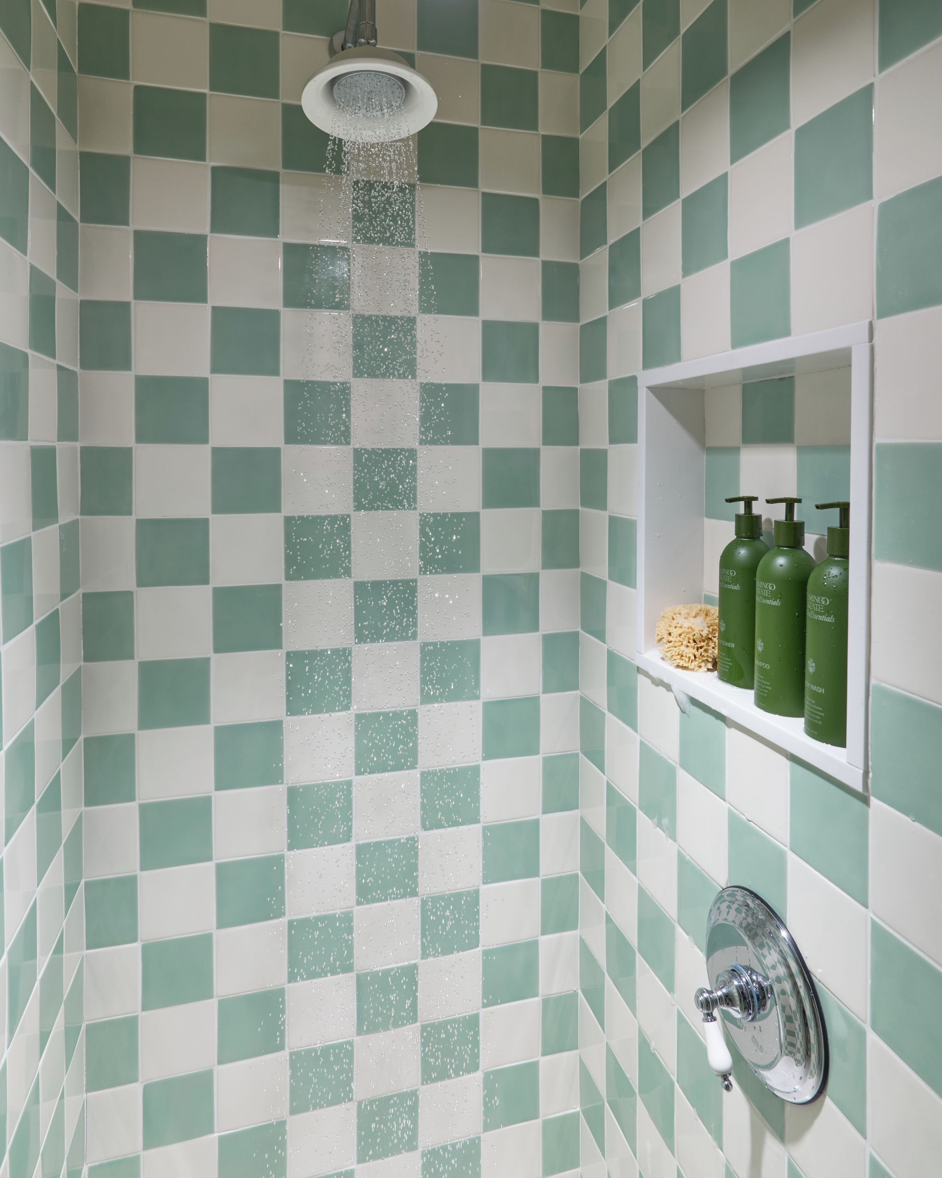 A shower with a checkered tile pattern and a shelf with green bottles.