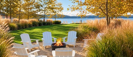 A beachside outdoor seating area with white Adirondack chairs and a fire pit.