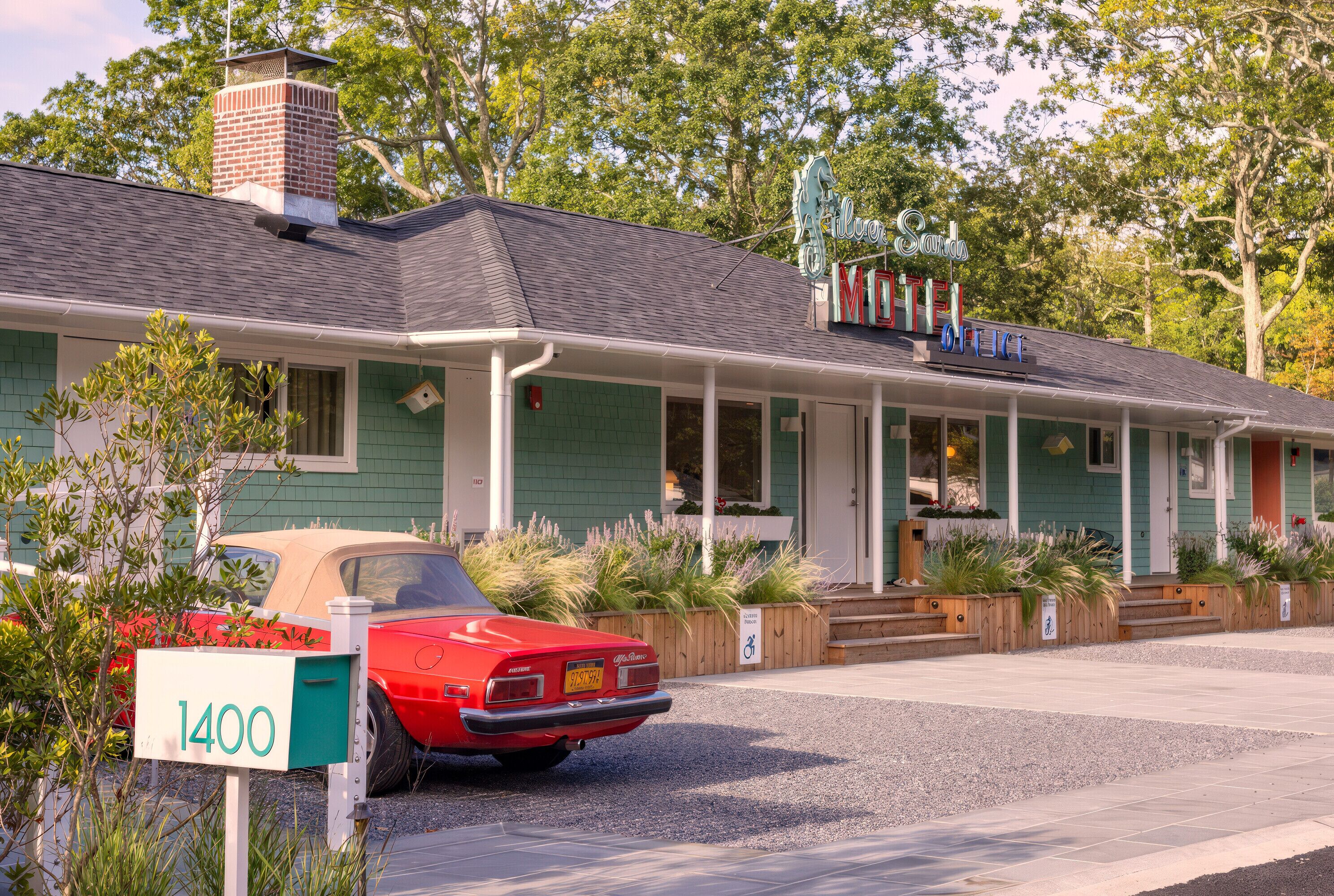 Un motel d’époque à la façade verdoyante, avec une voiture rouge classique garée devant, et une enseigne indiquant « Silver Star Motel ».