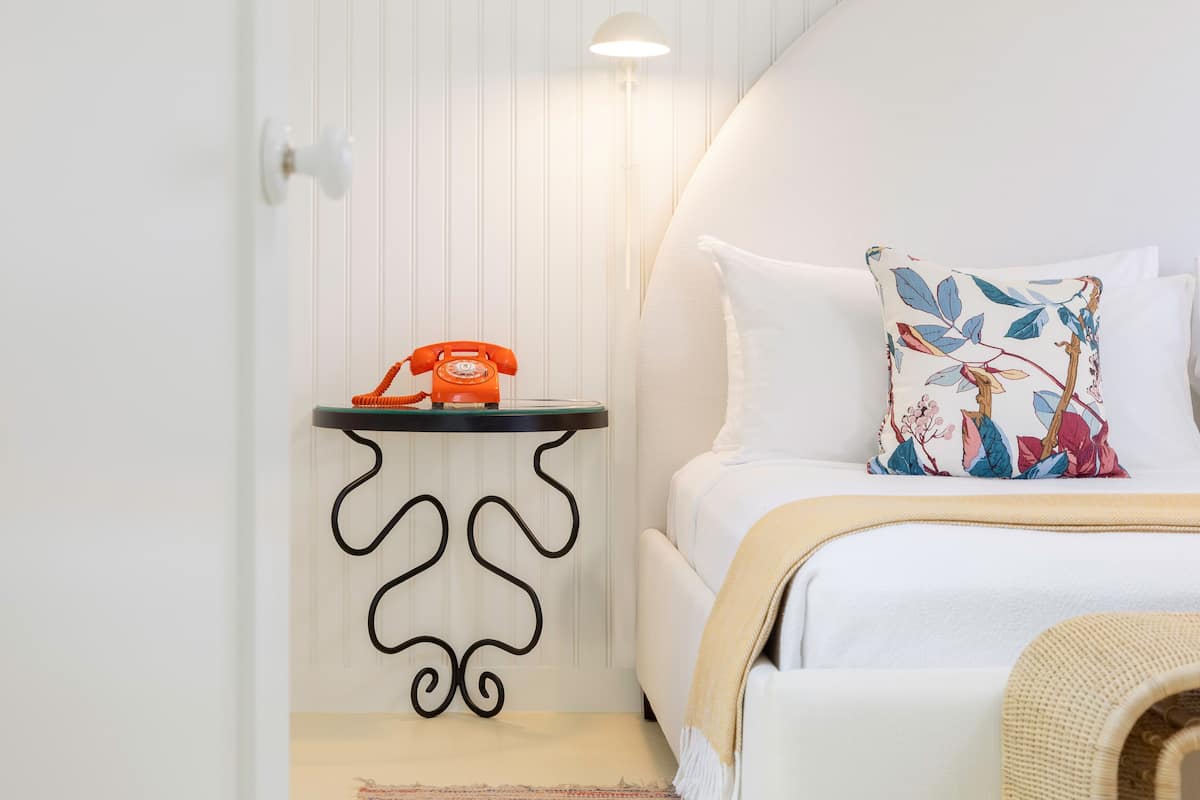 A neatly arranged bedroom with a bed, a bedside table with a telephone, and a wall-mounted light.