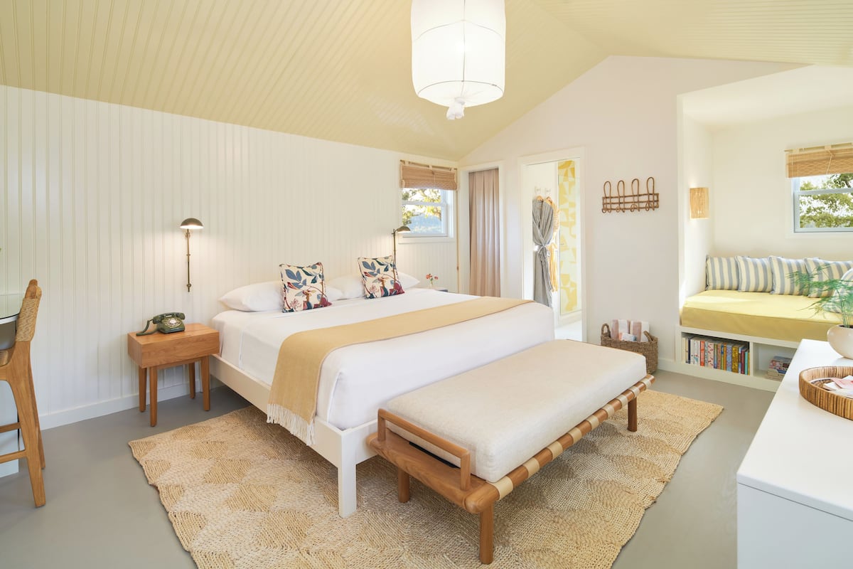 A bedroom with a large bed, bedside tables, a desk, and a reading nook with a sofa and books.