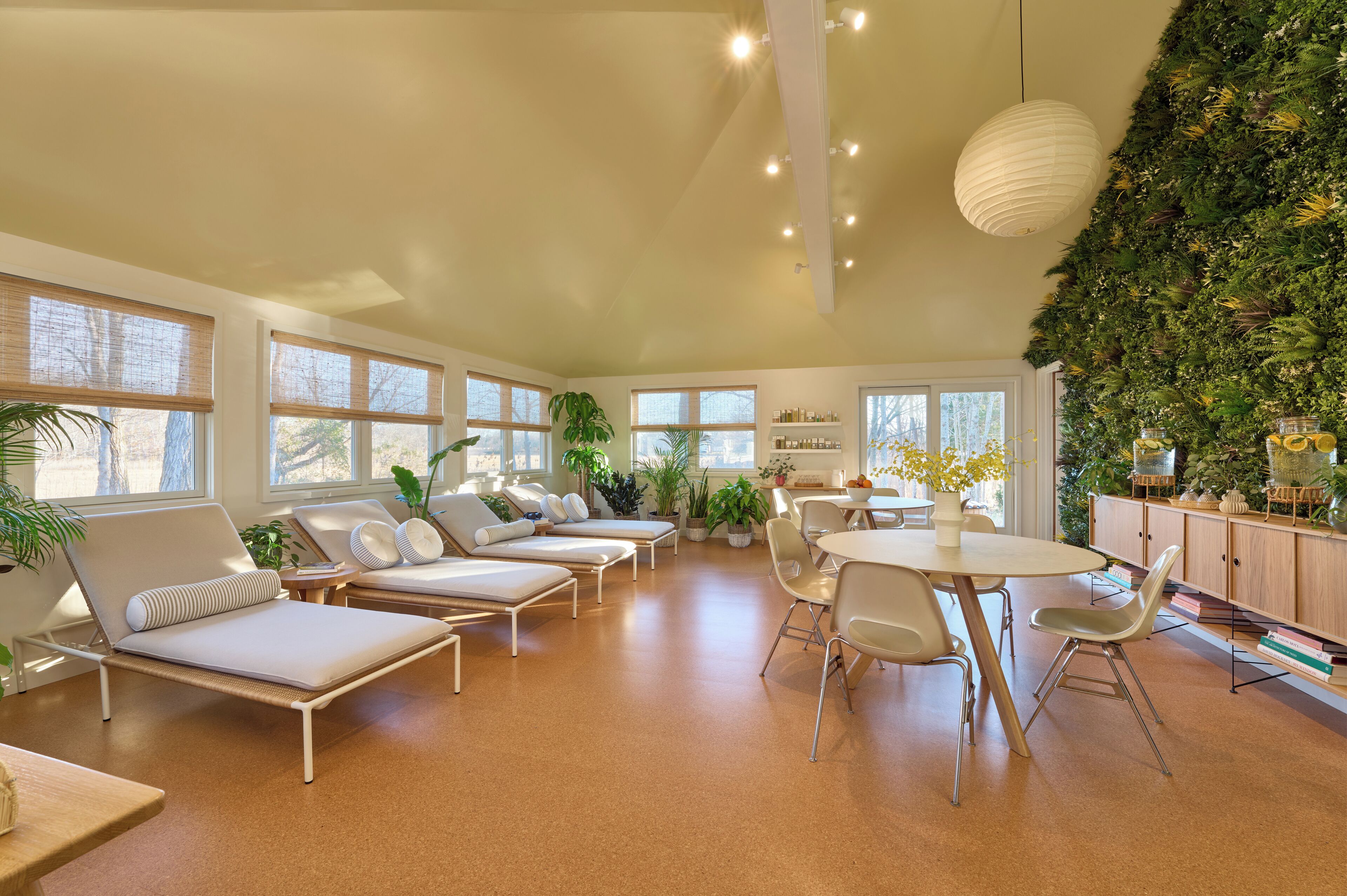 Un espacio lounge moderno con sillones blancos, una mesa redonda y una pared verde con plantas.