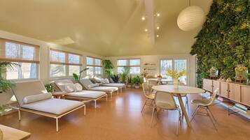 Un espacio lounge moderno con sillones blancos, una mesa redonda y una pared verde con plantas.