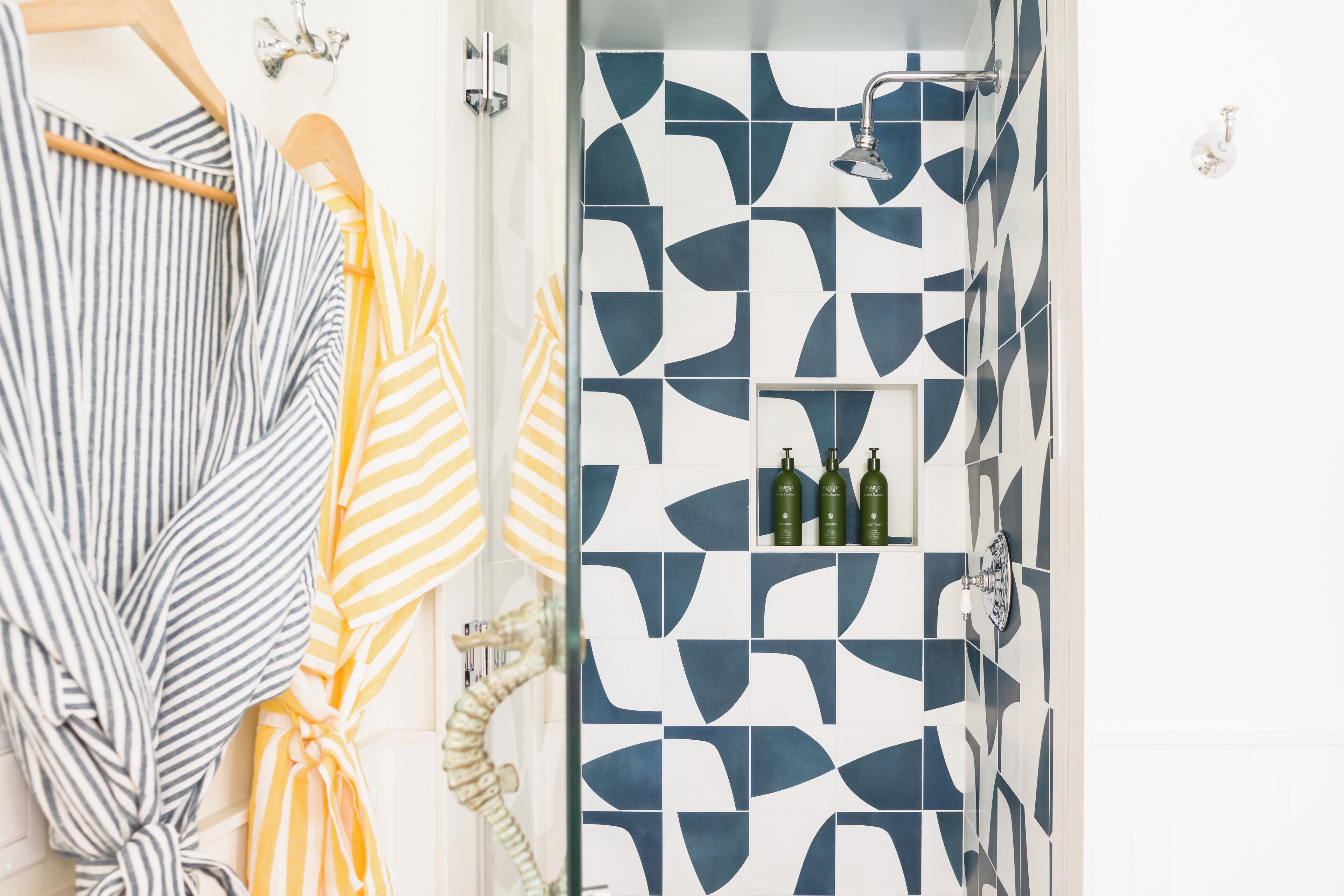 Une salle de bain avec un carrelage aux motifs géométriques, un porte-serviettes avec des serviettes à rayures et une douche équipée d’un pommeau de douche à main.