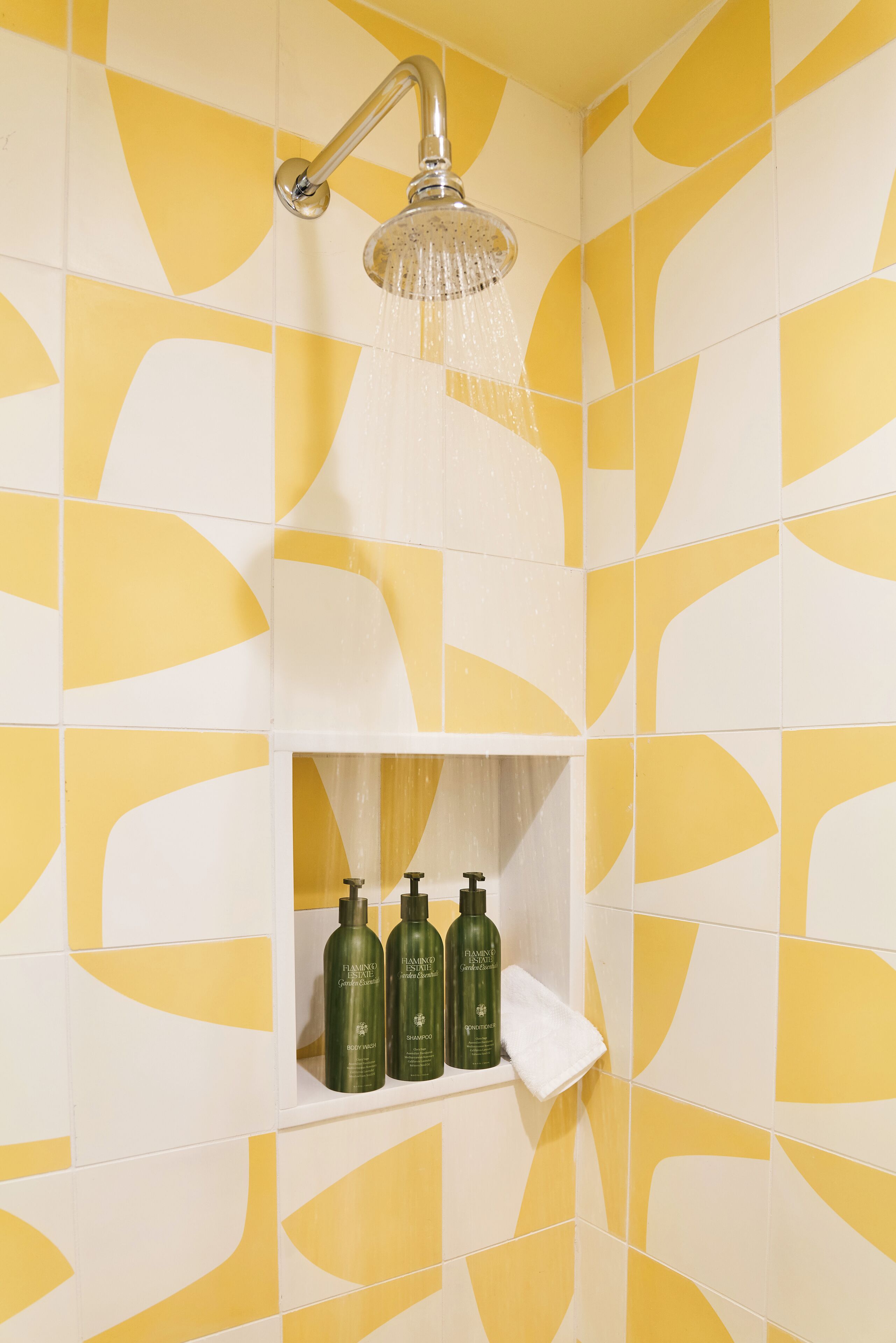 A shower with a handheld showerhead, a shelf with toiletries, and yellow and white patterned tiles.