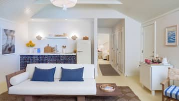 Una sala de estar moderna y bien iluminada, con un sofá blanco, una mesa de centro y una kitchenette al fondo.