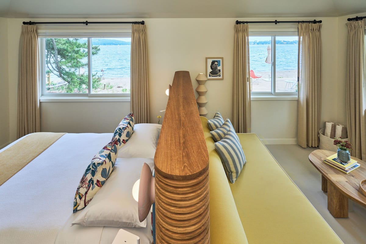A hotel room with a bed, a sofa, a wooden coffee table, and a view of the sea through large windows.