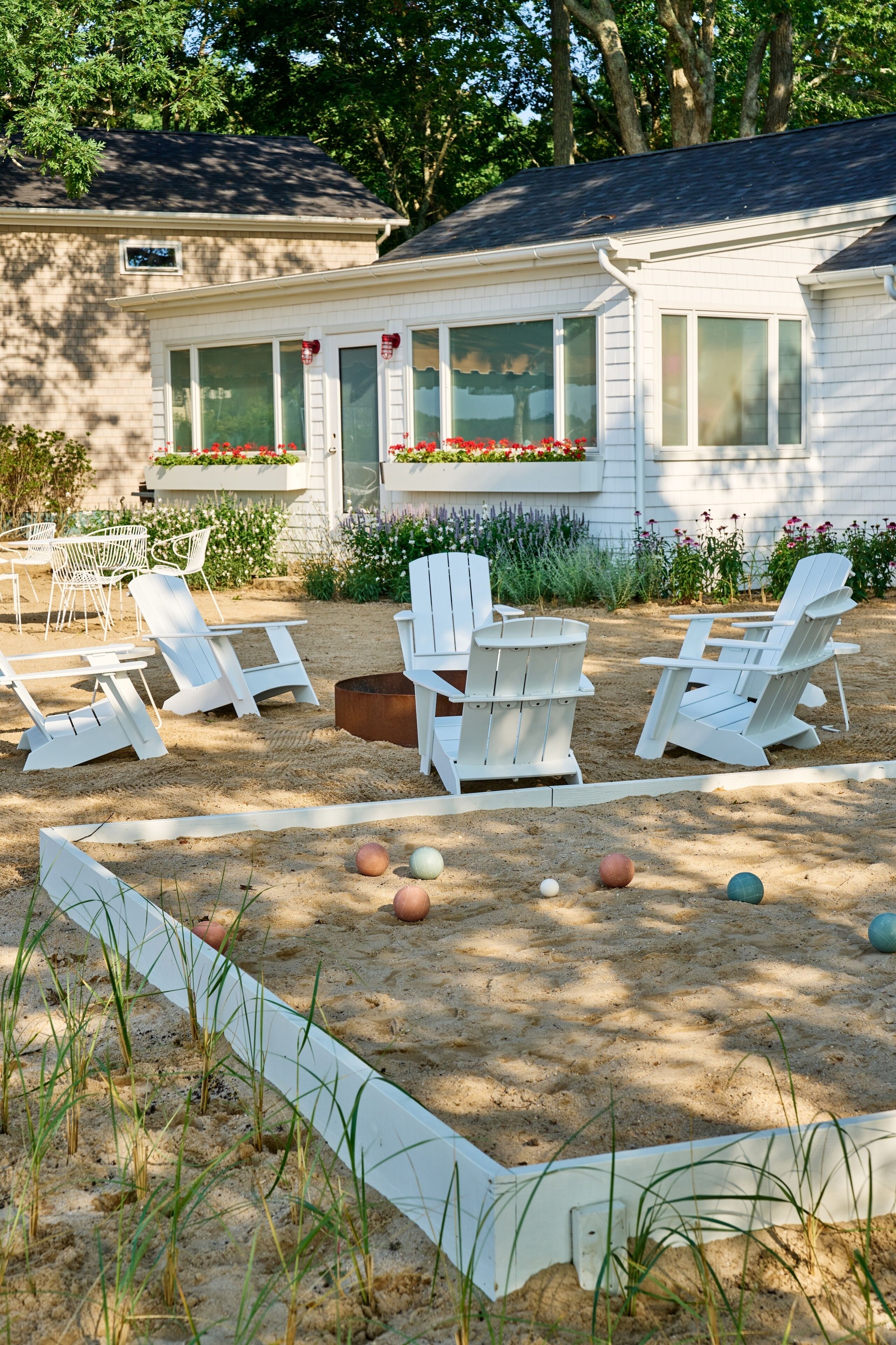 A house with a covered outdoor seating area featuring white Adirondack chairs and a sand garden with colorful balls.