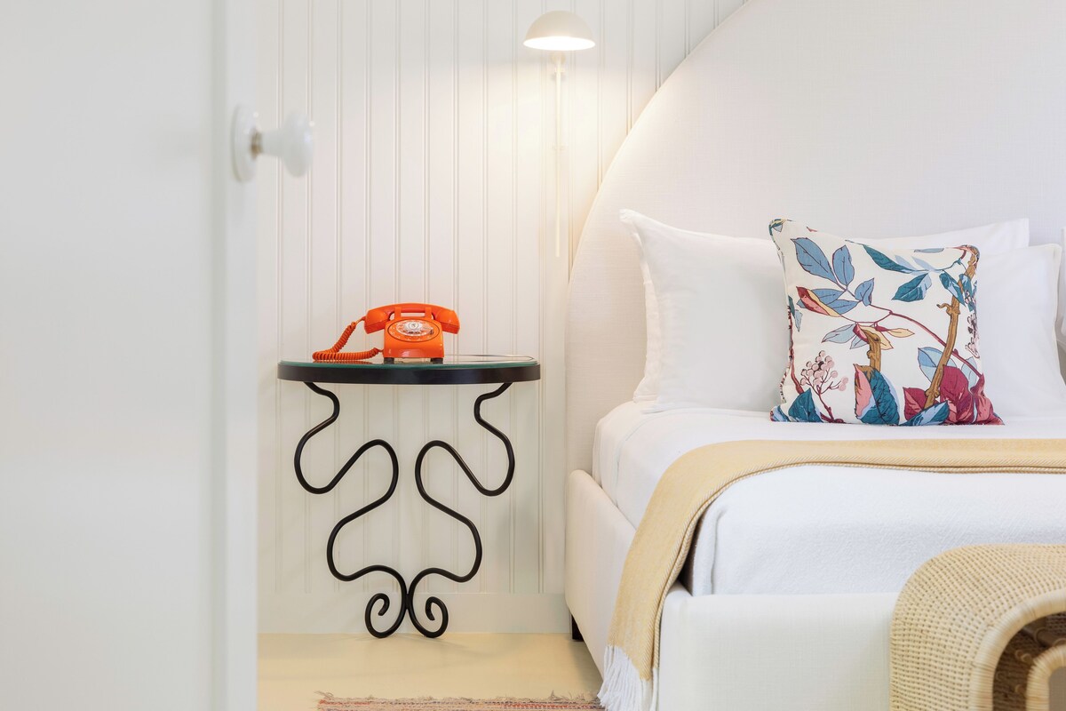 Un dormitorio ordenado con cama, una mesita de noche con teléfono y una lámpara de pared.