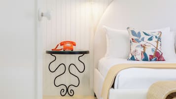 A neatly arranged bedroom with a bed, a bedside table with a telephone, and a wall-mounted light.