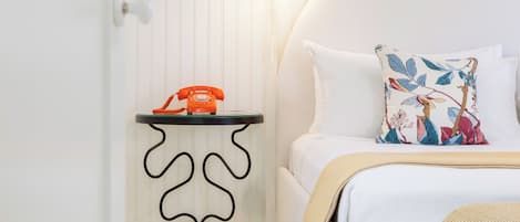 A neatly arranged bedroom with a bed, a bedside table with a telephone, and a wall-mounted light.