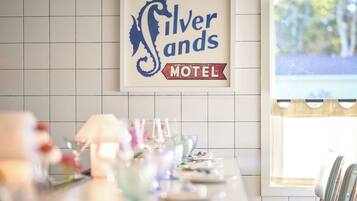 A hotel bar with a long counter, a sign reading "Silver Sands Motel," and a window with a view of trees.