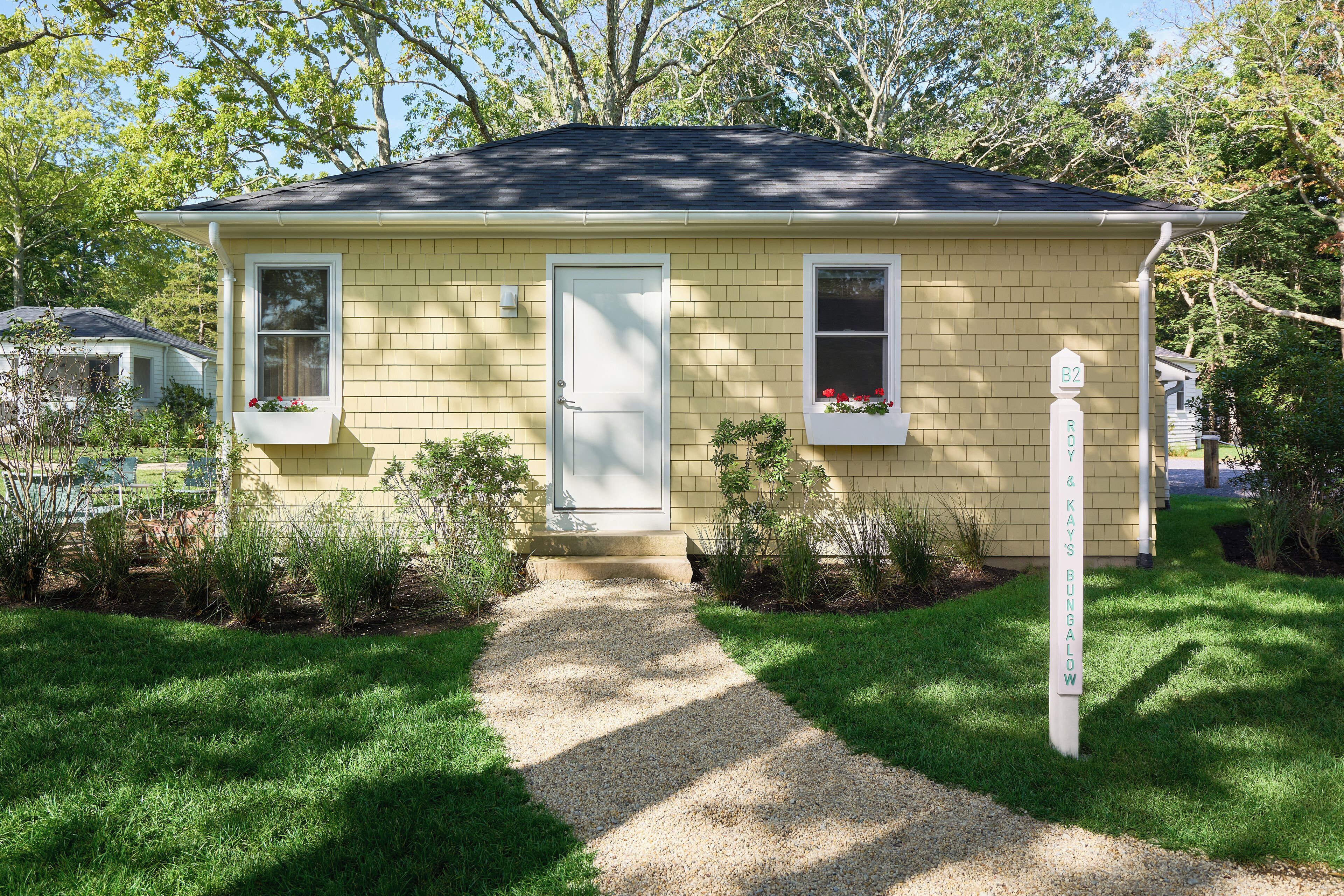 A yellow single-story house with a front door, two windows, and a gravel path leading to the door.