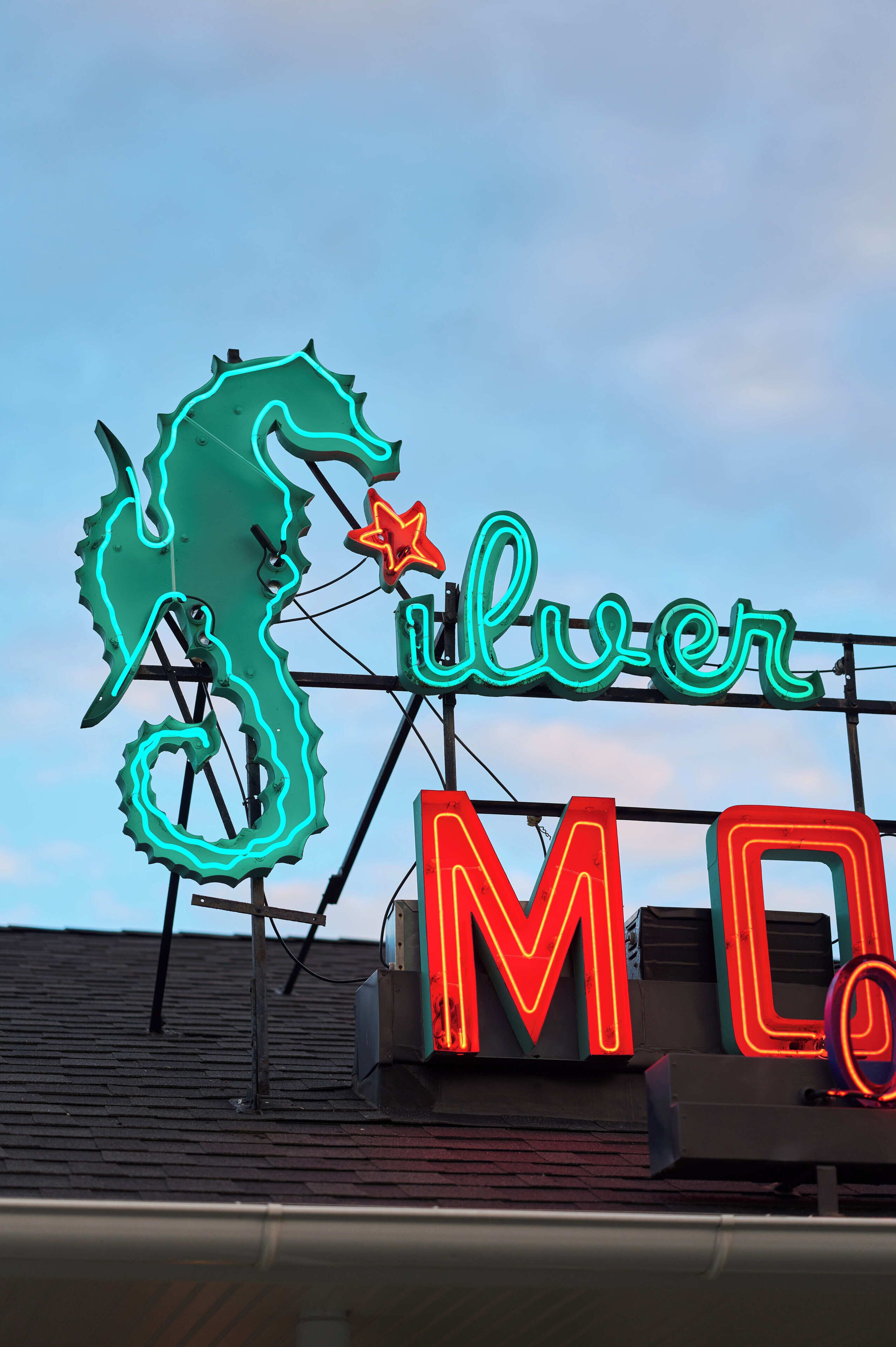 A neon sign with a seahorse and the word "Silver" on a rooftop.