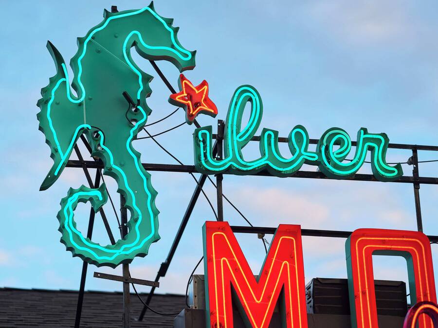 A neon sign with a seahorse and the word "Silver" on a rooftop.