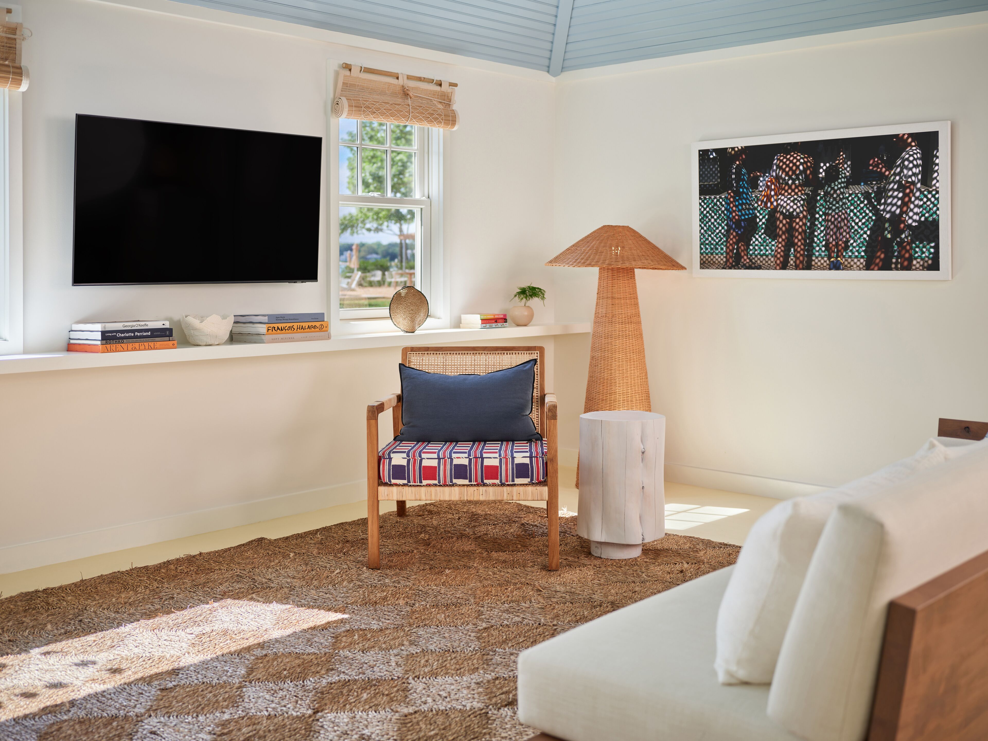 Una sala de estar con televisor, un sillón con cojín estampado, una lámpara de pie y un cuadro en la pared.