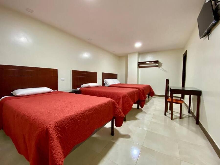 A hotel room with three beds, a desk, and a chair.