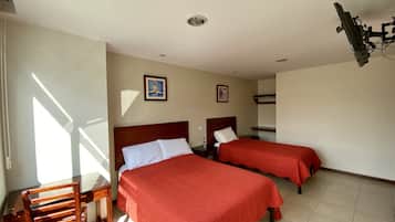 Una habitación de hotel con dos camas, una silla de madera, un escritorio y un ventilador de techo.
