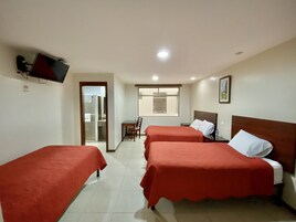 Habitación de hotel con dos camas individuales, un escritorio y televisión en la pared.