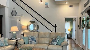 Amplia sala de estar con ventilador de techo alto, una escalera y vista a la casa de playa.
