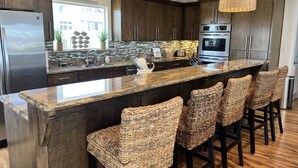 Una cocina moderna con armarios de madera oscura, una isla grande con taburetes de bar, electrodomésticos de acero inoxidable y un letrero de bienvenida.