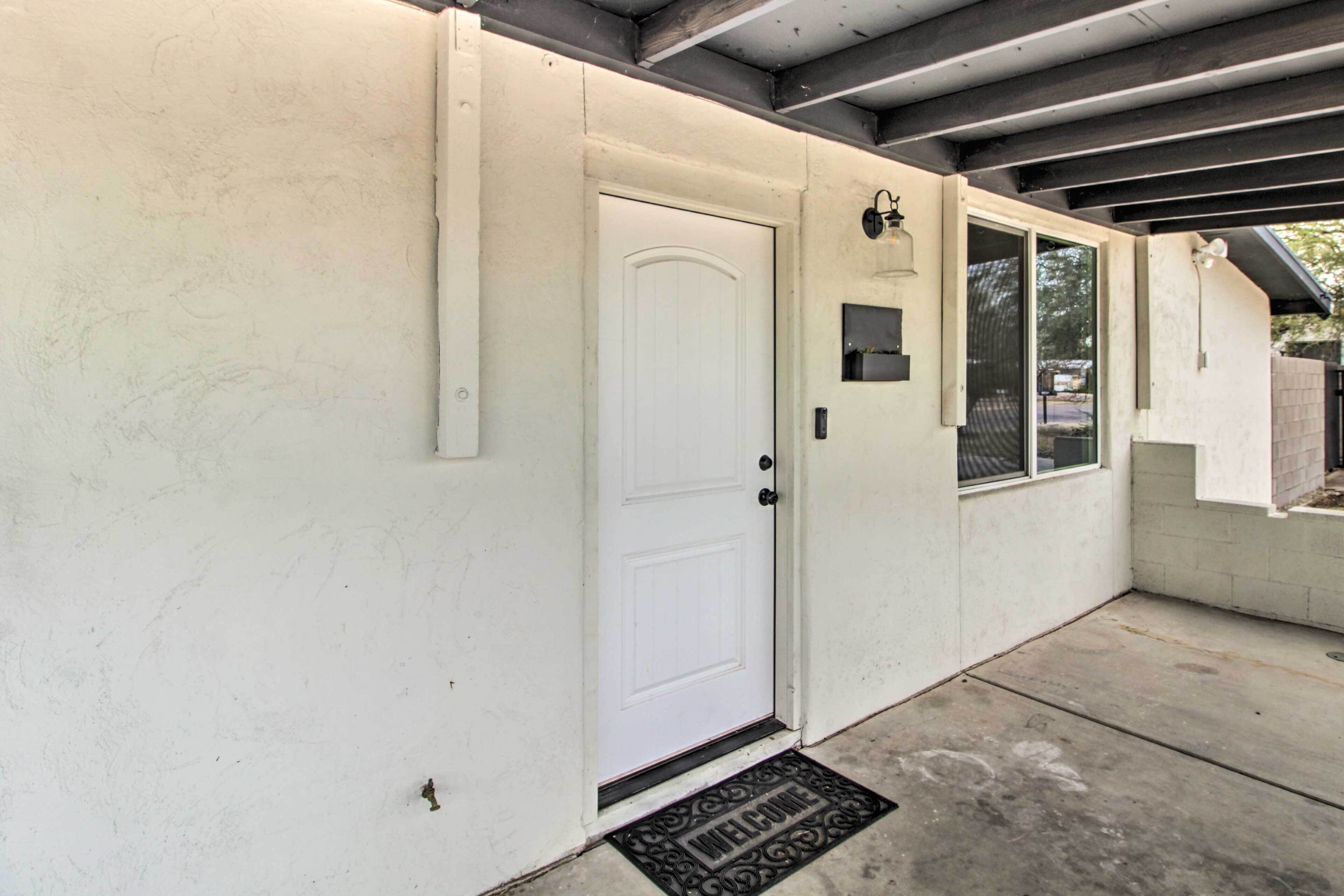 A white door with a doormat, a small window, and a wall-mounted light fixture.