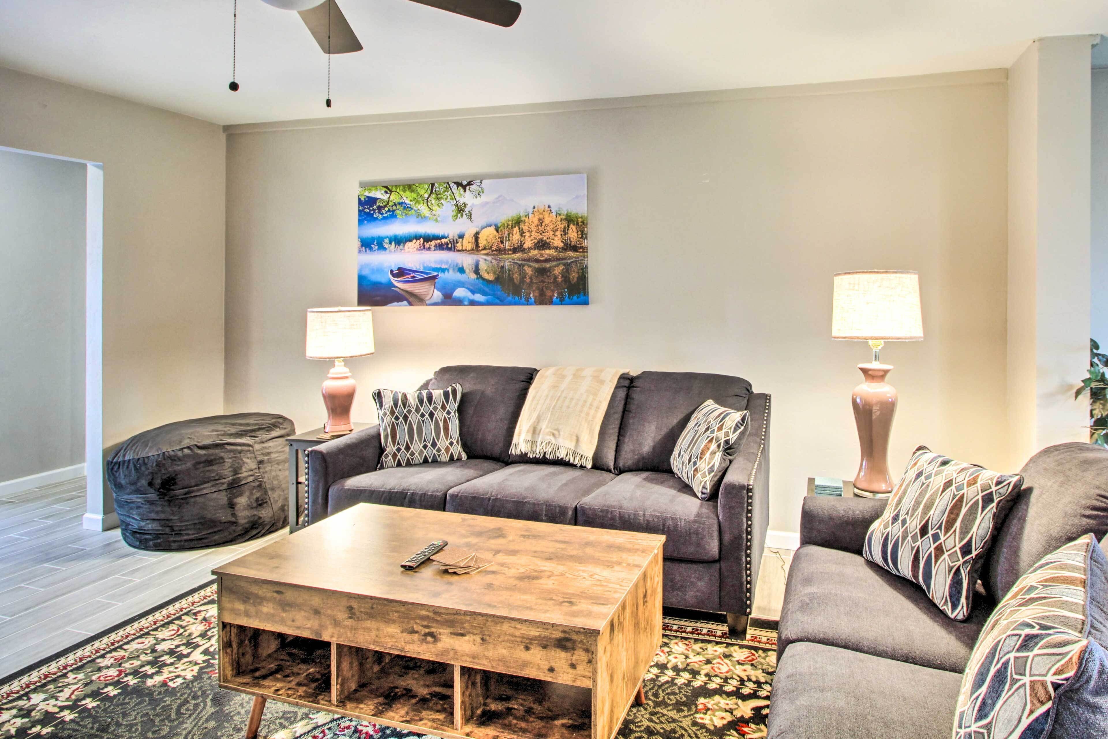 A living room with a gray sofa, two side tables with lamps, a wooden coffee table, and a large landscape painting on the wall.