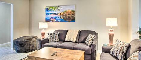 A living room with a gray sofa, two side tables with lamps, a wooden coffee table, and a large landscape painting on the wall.