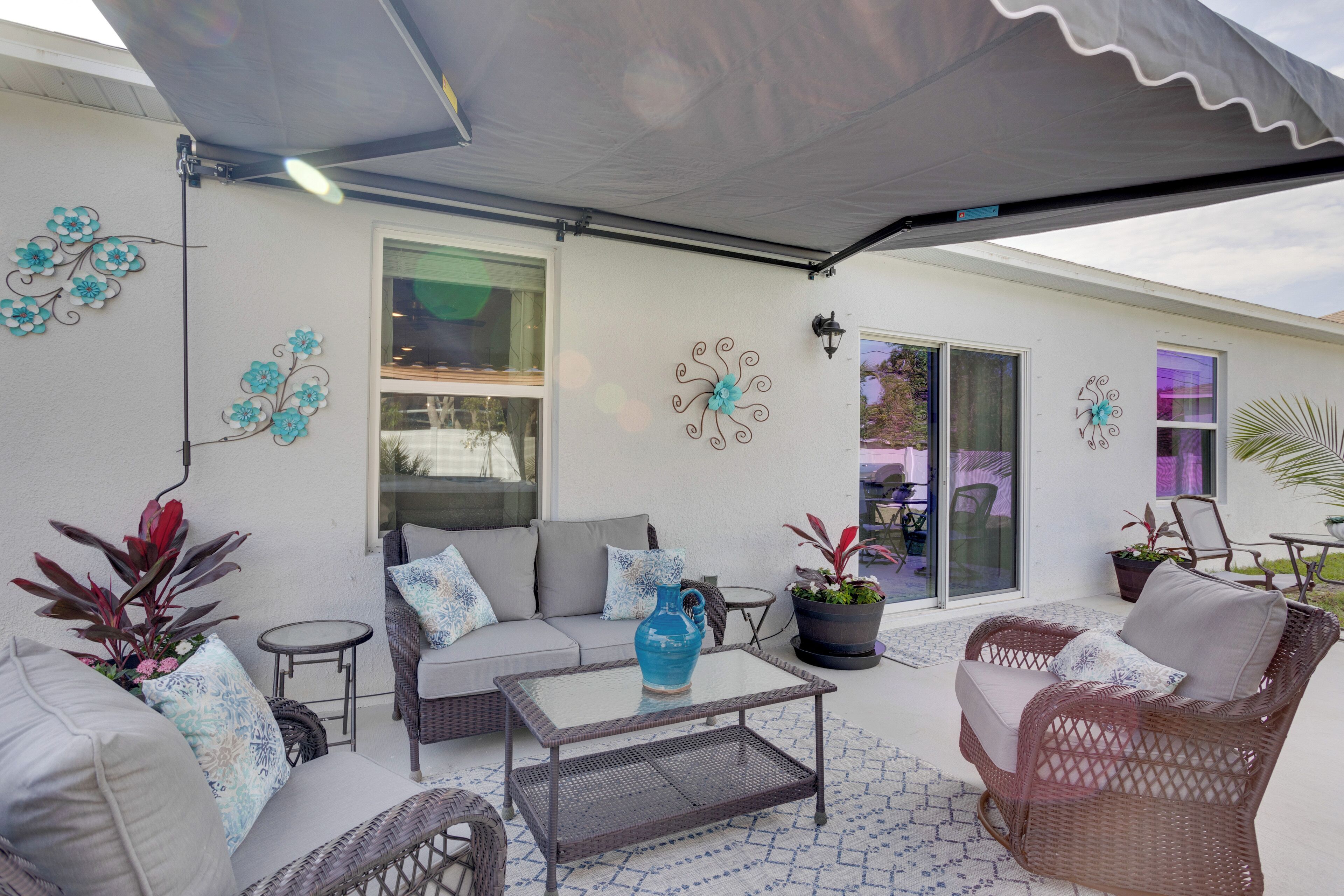 Un patio al aire libre con mobiliario de mimbre, una mesa de vidrio y decoración en la pared.