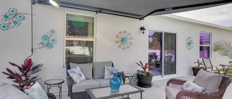 Un patio al aire libre con mobiliario de mimbre, una mesa de vidrio y decoración en la pared.