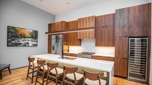 Une cuisine moderne avec des meubles en bois, un îlot central doté de tabourets, un réfrigérateur et un four encastré.