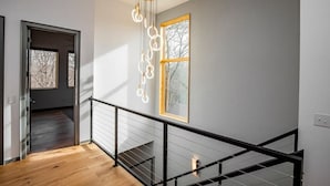 Un intérieur moderne avec un escalier, un luminaire suspendu et une fenêtre donnant sur des arbres.