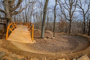 Un puente de madera en un bosque con árboles desnudos y un sendero de tierra.