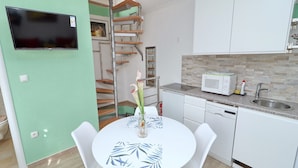 A compact kitchen with a microwave, sink, and white cabinets. A dining table with chairs is in the center.